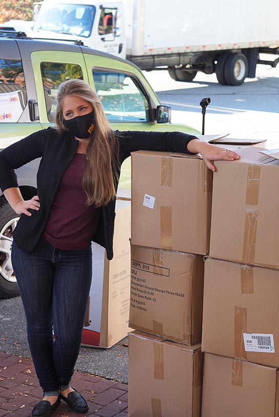 Laurie Camara, Manager of Hospitality Training and Education, RI Hospitality Association, poses with a stack of boxes filled with blankets during a brief respite from loading pallets and cars.